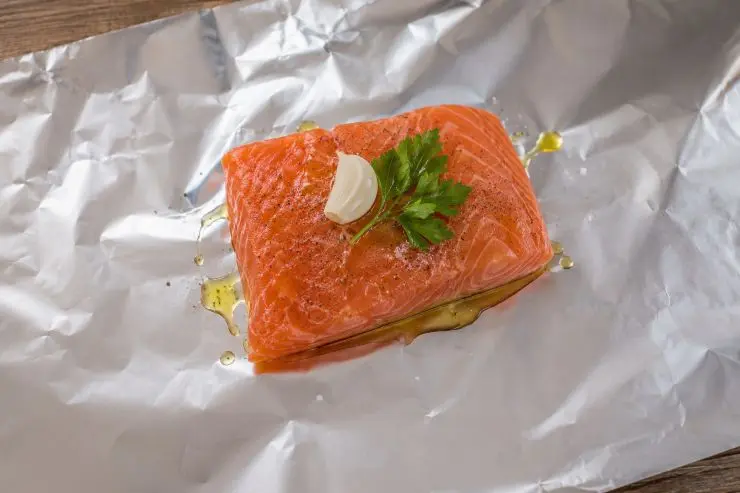 Adagiate il filetto di salmone su un foglio di alluminio per alimenti grande circa tre volte il filetto di salmone. Aggiungete uno spicchio di aglio, un rametto di prezzemolo, un pizzico di sale e, se lo gradite, un pizzico di pepe. Completate il tutto con un filo di olio extravergine di oliva.