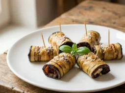 Sei involtini di melanzane grigliate disposti a raggiera su un piatto bianco, farciti con formaggio, guarniti con una foglia di basilico e chiusi con stuzzicadenti, su un tavolo di legno rustico.