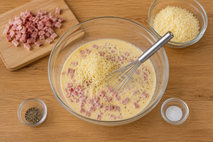 Tagliate il prosciutto a dadini o a listarelle e grattugiate il formaggio. In una ciotola versate le uova, sbattete bene, aggiungete la panna fresca, il pepe, il sale, il prosciutto e il formaggio grattugiato. Mescolate bene.