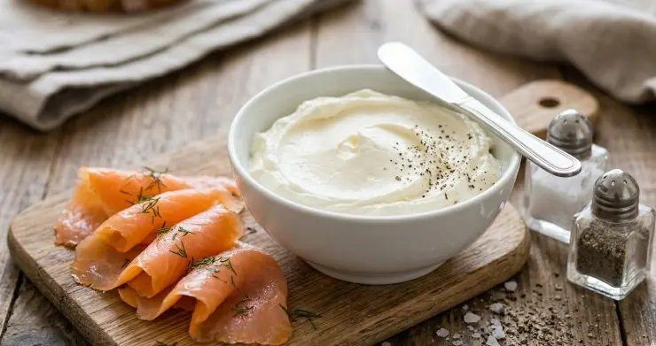 Su una spianatoria ponete le fette di salmone affumicato e tagliate e metà quelle che risultano troppo grandi. Adagiate sopra ogni fetta un abbondante cucchiano di formaggio e arrotolate il tutto in modo da formare una sorta di involtino con ogni fetta. Chiudete ciascun rotolino con un filo di erba cipollina.