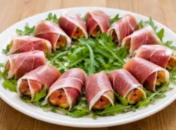 Piatto pronto da servire con fichi freschi avvolti nel prosciutto crudo e decorati con rucola fresca.