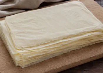 Pila di sfoglie di pasta fillo fatta in casa pronta per essere utilizzata su tagliere in legno.
