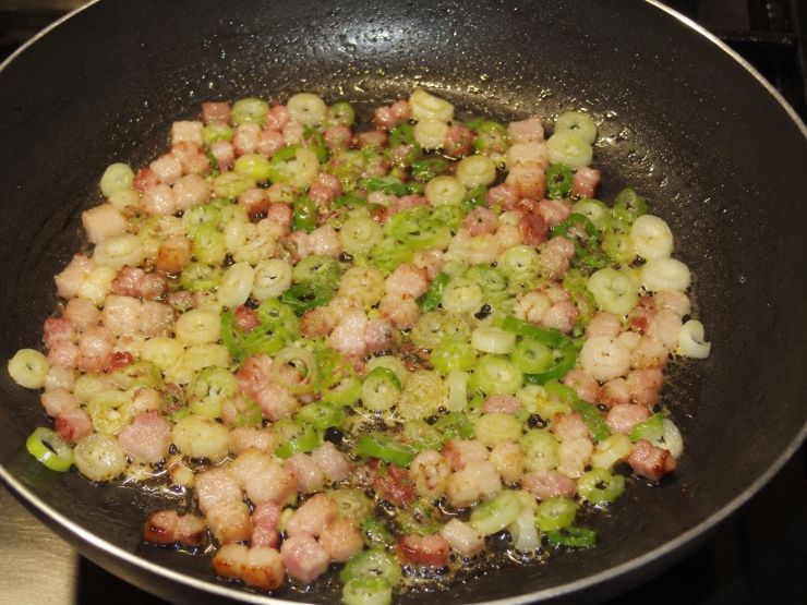 Pulite i cipollotti e affettateli in modo sottile, dopodiché metteteli a soffriggere in una padella antiaderente con due cucchiai di olio. Aggiungete la pancetta tagliata a dadini e fatela dorare per bene.