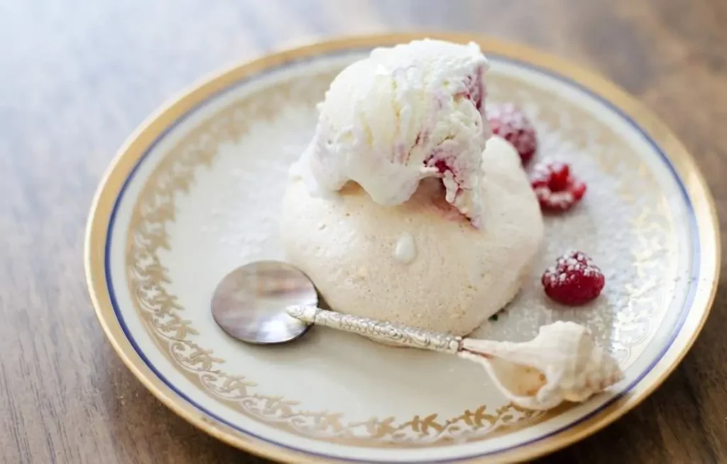 Mini pavlova con gelato Mini pavlova con gelato guarnita con lamponi freschi servita su un piatto elegante.