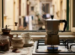Moka tradizionale sul fuoco in una cucina italiana con vista su un vicolo storico, vapore che esce dalla caffettiera.