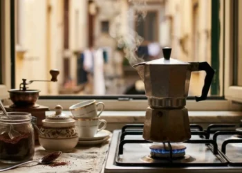 Moka tradizionale sul fuoco in una cucina italiana con vista su un vicolo storico, vapore che esce dalla caffettiera.