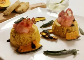 Sformatini di zucca con bacon e salvia impiattati su piatto bianco con decorazioni di salvia croccante e gocce di aceto balsamico