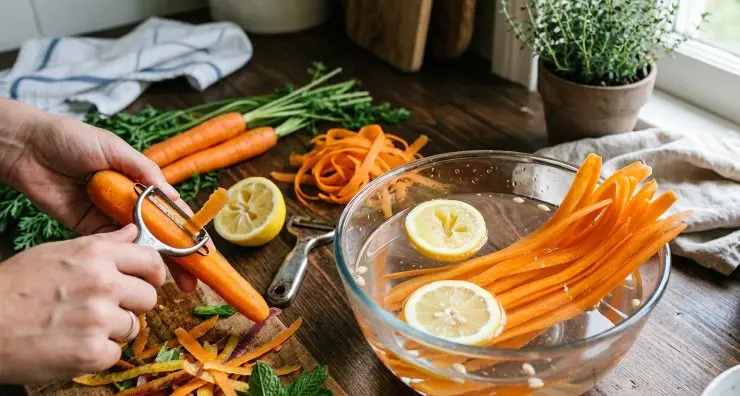 Versate l‘acqua fredda in una ciotola. Spremete nell’acqua il succo di mezzo limone, tagliatene una fetta e aggiungetela all’acqua nella ciotola. Lavate e sbucciate le carote. Usando il pelapatate continuate a tagliare delle strisce sottili di carota. Mettete le tagliatelle ottenute in questo modo nella ciotola con il limone.
