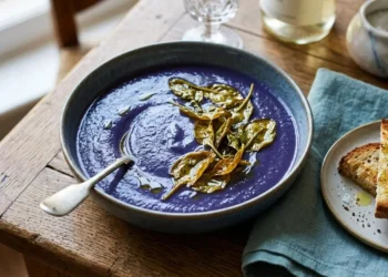 Vellutata di cavolo rosso viola brillante in ciotola decorata con spinaci croccanti e servita con crostini di pane