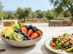 Composizione di frutta fresca con kiwi, ananas e fragole accanto a un piatto unico bilanciato su un tavolo all'aperto, concetto di nutrizione sana 2026.