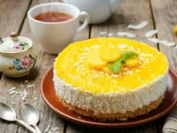 Cheesecake al mango fresca senza cottura decorata con scaglie di cocco e menta su un tavolo in legno