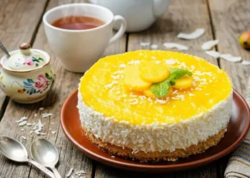 Cheesecake al mango fresca senza cottura decorata con scaglie di cocco e menta su un tavolo in legno