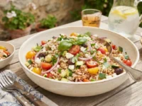 Insalata di farro e orzo fredda in una ciotola di ceramica su una tavola estiva all'aperto