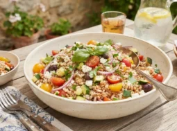 Insalata di farro e orzo pronta da servire Insalata di farro e orzo fredda in una ciotola di ceramica su una tavola estiva all'aperto
