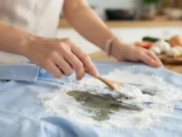 Persona che applica l'amido di mais con un cucchiaio su una macchia d'olio in una camicia azzurra.