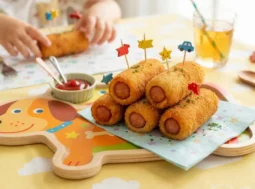 Rollini di wurstel croccanti e dorati serviti su un piatto colorato a misura di bambino, pronti da gustare