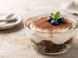 Tiramisù light estivo in coppetta Coppetta di tiramisù light estivo guarnita con cacao e mirtilli freschi su sfondo in legno