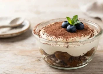 Coppetta di tiramisù light estivo guarnita con cacao e mirtilli freschi su sfondo in legno