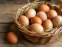 Cesta di vimini colma di uova fresche adagiate sulla paglia e appoggiata su un tavolo di legno rustico illuminato da luce naturale.