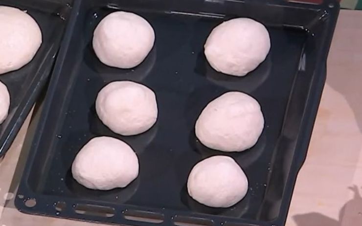 Ripiegate ogni panetto su se stesso portando i lembi esterni verso l’interno, così da ottenere delle palline lisce. Disponetele su una teglia ben distanziate, copritele e lasciatele lievitare ancora per 1 ora e mezza. Fatto ciò infarinate leggermente il piano di lavoro e distribuite le palline di impasto. Ripiegate ogni panetto su se stesso portando i lembi esterni verso l’interno, così da ottenere delle palline lisce. Disponetele su una teglia ben distanziate, copritele e lasciatele lievitare ancora per 1 ora e mezza. Fatto ciò infarinate leggermente il piano di lavoro e distribuite le palline di impasto.