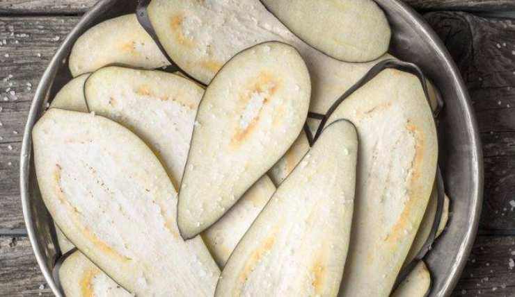 Iniziate lavando ed asciugando le melanzane: spuntatele e tagliatele a fette non troppo sottili, quindi disponetele in uno scolapasta alternando ad una spolverata di sale. Lasciatele riposare così con un peso sulla superficie, in modo che possano rilasciare quanta più acqua di vegetazione possibile: in questo modo andrete ad eliminare quel retrogusto amaro che può non piacere.