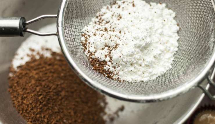 Procedete ora incorporando gradualmente gli ingredienti secchi setacciati a quelli liquidi: un cucchiaio per volta e senza smettere di amalgamare, in modo da evitare la formazione di grumi. Una volta ottenuto un composto morbido ed uniforme, aggiungete anche le gocce di cioccolato fondente con una spatola, distribuendole bene nell’impasto.Versate il tutto in una teglia rivestita di carta da forno bagnata e strizzata, livellate la superficie.