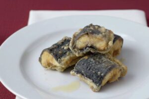 pezzi di capitone appena fritto in un piatto su tavolo con tovaglia rossa