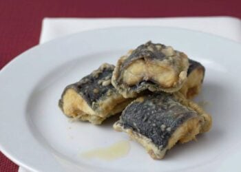 pezzi di capitone appena fritto in un piatto su tavolo con tovaglia rossa