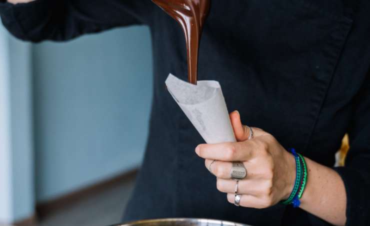 Una volta fuso il cioccolato prepariamo una teglia e foderiamola con la carta da forno. Riempiamo la sac a poche col cioccolato, assicurandoci di usare il beccuccio più stretto e sottile a disposizione. Se non abbiamo una classica sac a poche possiamo farla con la carta da forno dando una forma a imbuto;