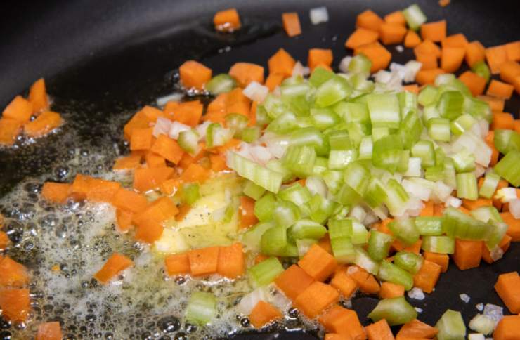 Andiamo quindi a tagliare la carne a pezzetti più piccoli. Prepariamo un tegame capiente e al suo interno versiamo un paio di giri abbondanti di olio d’oliva. Accorpiamo il trito di sedano e carote e scaldiamo. Uniamo le cipolle e lasciamo soffriggere qualche minuto;