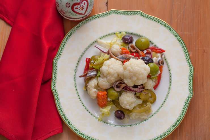 A questo punto, versa il cavolfiore in una scodella, aggiungi le papacelle, la giardiniera scolata, le olive denocciolate, le acciughe e i capperi dissalati e condisci tutto con olio extravergine d’oliva e aceto. Regola di sale e mescola bene. Infine, lasica riposare l’insalata di rinforzo in frigorifero per un’oretta prima di servirla.