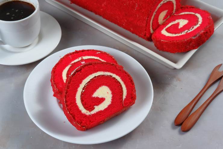 Quando la pasta biscotto sarà completamente fredda, capovolgila su un piano da lavoro, eliminando la carta da forno, e spalmaci sopra la crema. Arrotola la base su se stessa partendo dal lato più corto ed avvolgila in un altro foglio di carta da forno. Lasciala riposare in frigo per 30 minuti e infine tira fuori il tuo rotolo Red Velvet, estrailo dall’involucro, cospargilo lo con zucchero a velo e taglialo a fette.