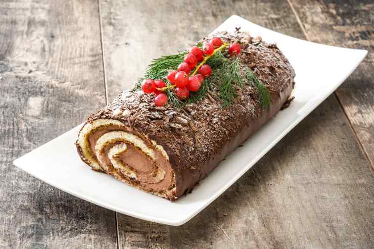 Trascorso il tempo necessario, riprendi la ganache, montala un poco con le fruste elettriche e spalmane un poco sulla base di pasta biscotto. Arrotola quest’ultima su se stessa ed avvolgila nella pellicola trasparente. Lascia il rotolo in frigo per 60 minuti e, successivamente, riprendilo e decoralo esternamente con la ganache rimasta. Aggiungi in superficie qualche scaglia di cioccolato e del ribes fresco e conserva il tronchetto in frigo fino al momento di servire.