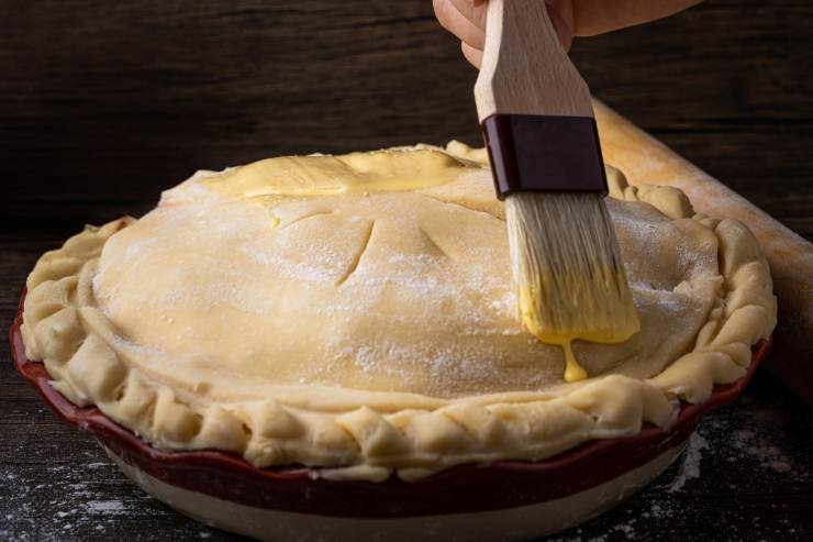 Sigilla bene i bordi, formando una sorta di cornicione. Pratica dei fori in superficie con i rebbi di una forchetta oppure delle incisioni con un coltello, così che il vapore esca durante la cottura, e poi spennella con un tuorlo d’uovo sbattuto.