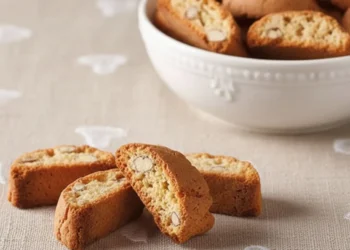 Cantucci toscani alle mandorle disposti su tovaglia rustica beige con cuori ricamati e ciotola bianca