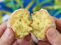 Mani che aprono una castagnola di Carnevale soffice ricoperta di zucchero con vassoio di dolci sullo sfondo