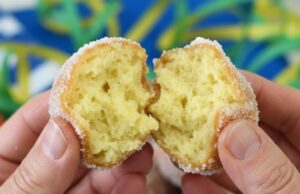 Mani che aprono una castagnola di Carnevale soffice ricoperta di zucchero con vassoio di dolci sullo sfondo