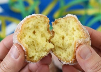 Mani che aprono una castagnola di Carnevale soffice ricoperta di zucchero con vassoio di dolci sullo sfondo