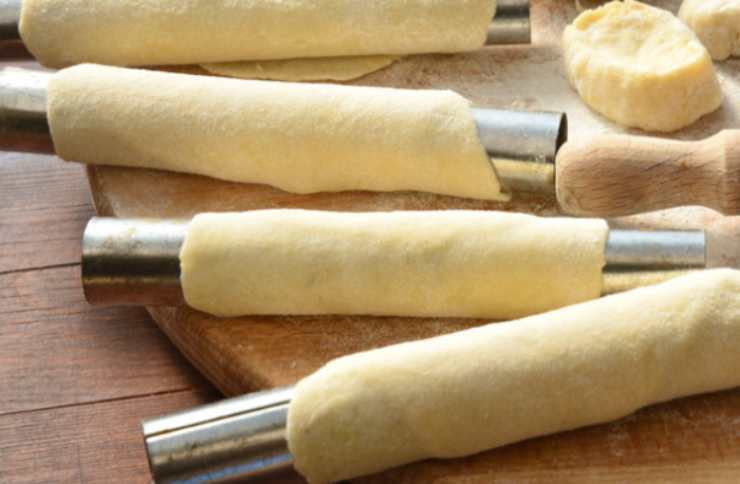 Assicuriamoci di arrotolare la striscia di sfoglia in modo che non restino “buchi” tra un giro e l’altro. Adagiamo i finti cannoli in una teglia da forno foderata e spennelliamoli su tutti i lati con un goccio di latte a temperatura. Spolveriamo adesso con lo zucchero di canna e inforniamo a 180 gradi.