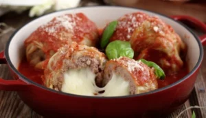 Piatto di involtini di verza al sugo di pomodoro con cuore di mozzarella filante, guarnito con basilico fresco
