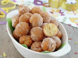 Vassoio di castagnole fritte di Carnevale con zucchero, mascherina e stelle filanti su tavolo in legno.