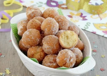 Vassoio di castagnole fritte di Carnevale con zucchero, mascherina e stelle filanti su tavolo in legno.