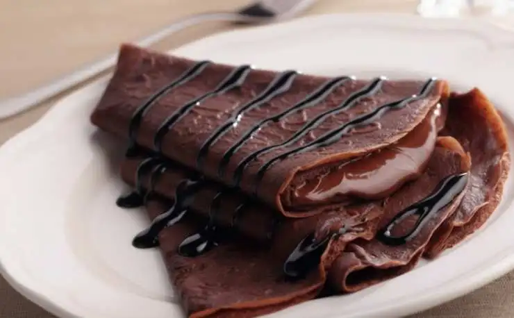 Ripetiamo per tutte le crepes. Intanto sciogliamo il cioccolato fondente a bagnomaria. Una volta fuso uniamo un cucchiaino di burro e mescoliamo per sciogliere. Riversiamo due o tre cucchiaini di cioccolato fondente al centro di ogni crepes e ripieghiamo a portafoglio. Spolveriamo con lo zucchero a velo et voilà.