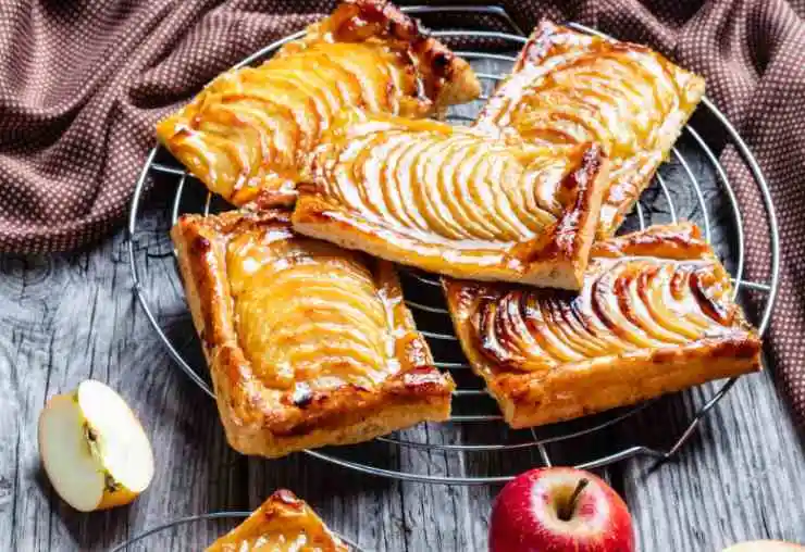 Ripieghiamoli leggermente sulle fettine di mela. Spolveriamo con un po’ di zucchero di canna le sfogliatine e inforniamo a 180 gradi e facciamo cuocere per 10/12 minuti fino a quando non saranno ben dorate.