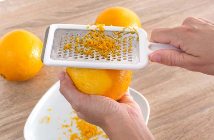 Uniamo la scorza grattugiata di arancia e il cucchiaio di succo di arancia e mescoliamo ancora. Riversiamo il composto in uno stampo da forno dai bordi alti e rettangolare che avremo foderato e livelliamo;