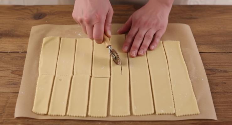 Trascorso il tempo necessario, dividete il panetto in pezzi e passateli nella macchina per la pasta. Partite dallo spessore più largo e scendete gradualmente fino all’ultimo o penultimo scatto: la sfoglia deve essere sottilissima. Con una rotella dentellata, ricavate dei rettangoli o dei rombi e praticate uno o due tagli centrali su ogni pezzo: aiuterà la chiacchiera a non arricciarsi troppo e a cuocere uniformemente.