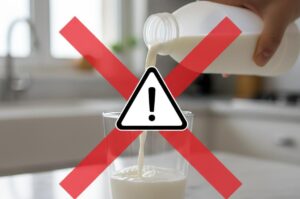 Una mano versa latte da una bottiglia bianca in un bicchiere di vetro, con un grande segnale di pericolo giallo sovrapposto per indicare un richiamo alimentare