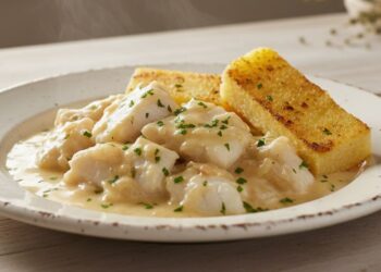 Piatto di baccalà alla vicentina cremoso con polenta grigliata, guarnito con prezzemolo fresco, in un'ambientazione rustica e luminosa.