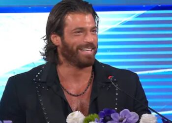 Can Yaman sul palco del Festival di Sanremo 2026 in abito elegante scuro mentre sorride al pubblico dell'Ariston, simbolo della sua incredibile forma fisica.