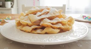 Gran vassoio di chiacchiere senza glutine dorate e piene di bolle su un tavolo decorato per Carnevale